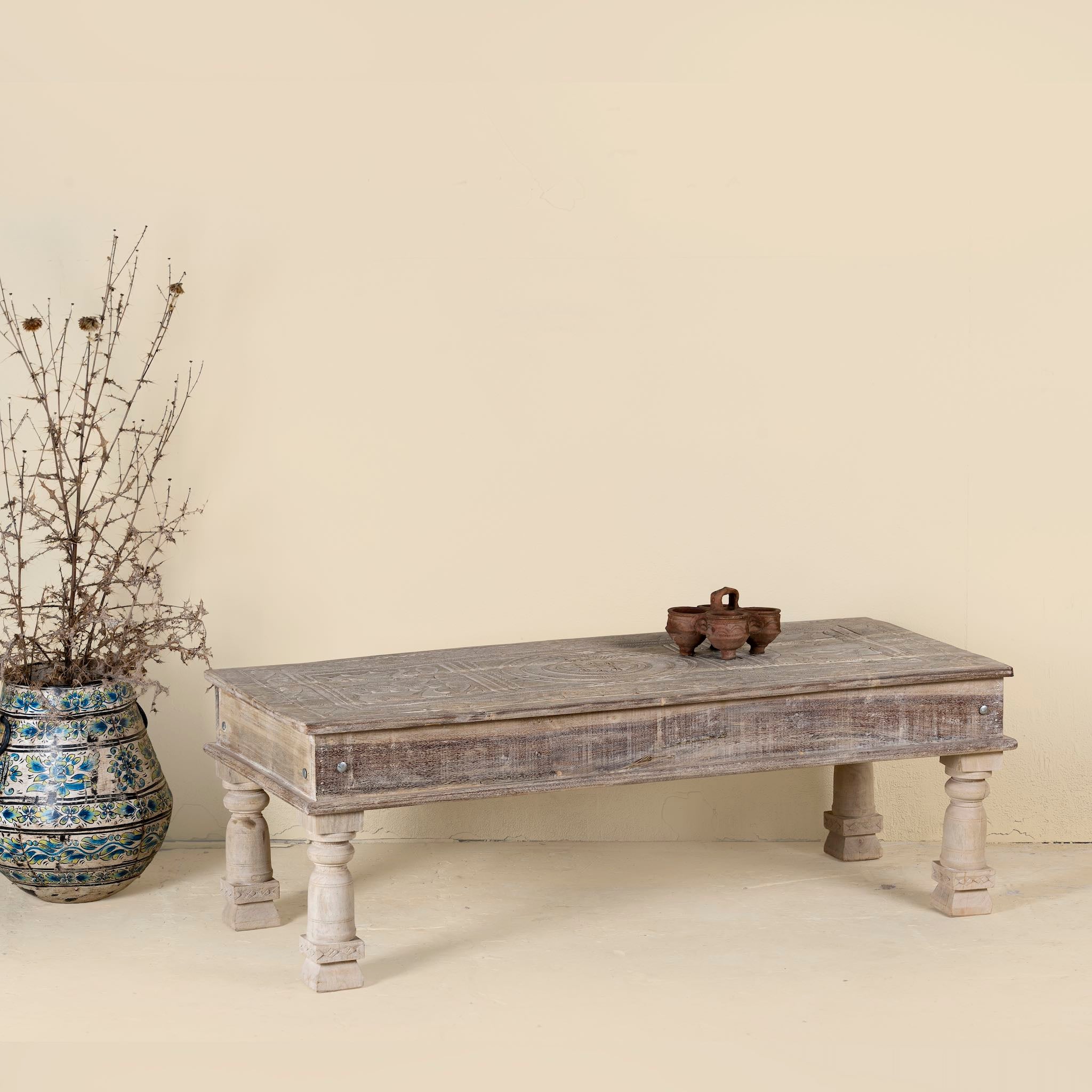 Rustic coffee table made from reclaimed teak wood, featuring hand-carved details on the tabletop and solid turned legs for a timeless, vintage look.
