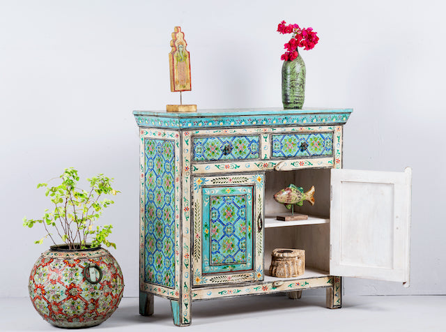 Side angle image with open doors of a vintage hand painted furniture cupboard in reclaimed wood with floral and geometric motifs, off-white distressed finish, 90 × 40 × 90 cm.
