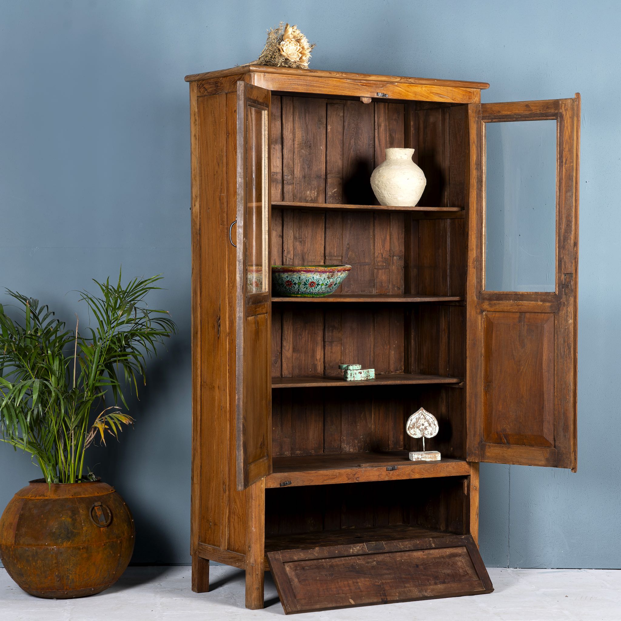 Side angle image with open door of a tall reclaimed teak wood display cabinet with two glass doors and a bottom drawer – wooden display cabinet crafted as sustainable furniture with natural elegance.