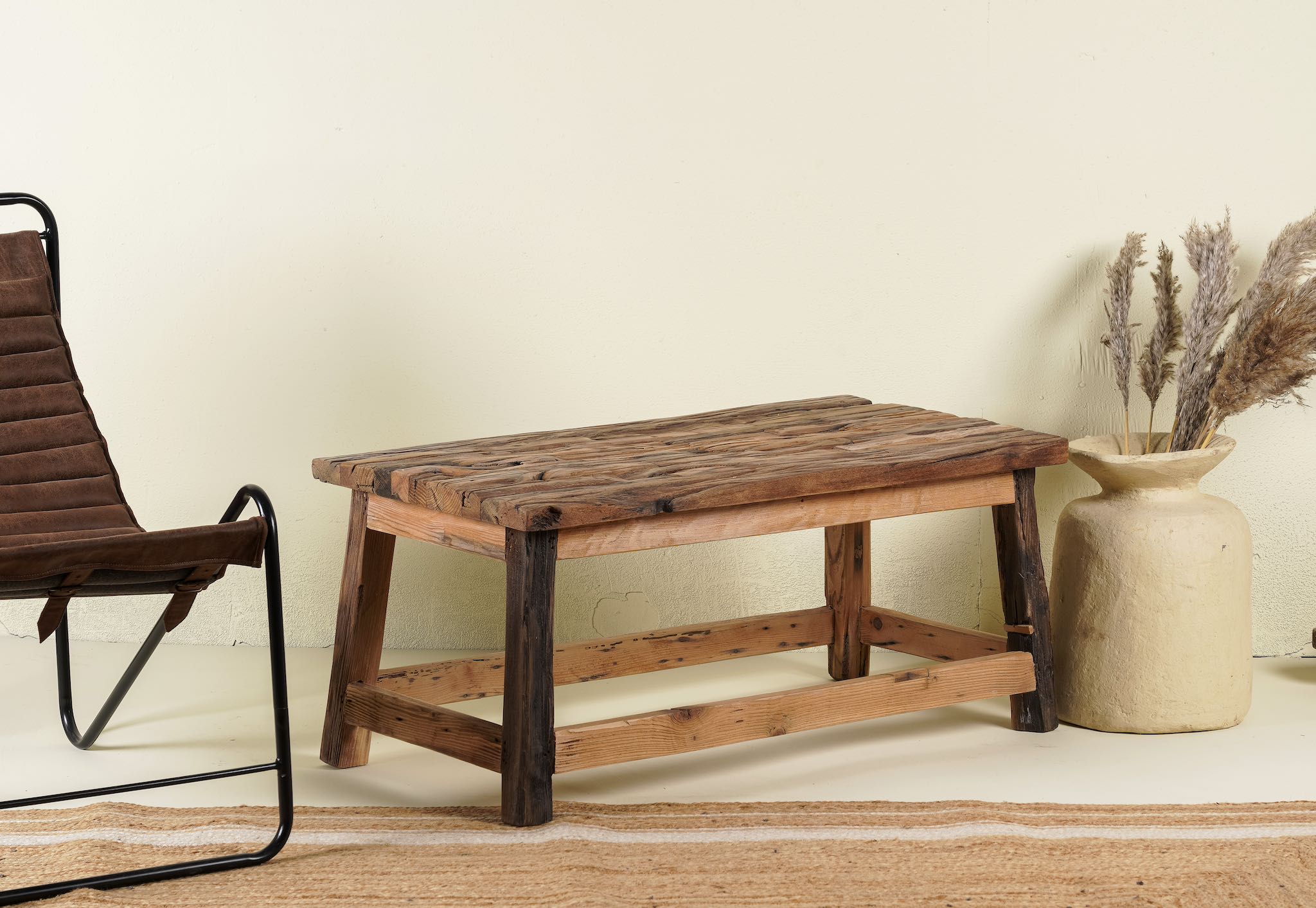 Side angle image of a rustic-style coffee table made from driftwood, showcasing a textured, uneven surface with natural wood tones and grain variations, supported by a sturdy, simple wooden frame, styled in a cozy minimal setting with neutral decor.

