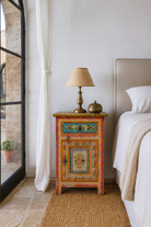 Lifestyle scene of a set of two hand painted bedside tables with floral motifs; sustainable furniture made of recycled wood, 45 × 35 × 70 cm.