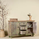 Side angle image with open door of a carved wooden furniture sideboard with floral hand-carving and distressed finish, vintage style cabinet made from mango wood, 150 × 40 × 90 cm.
