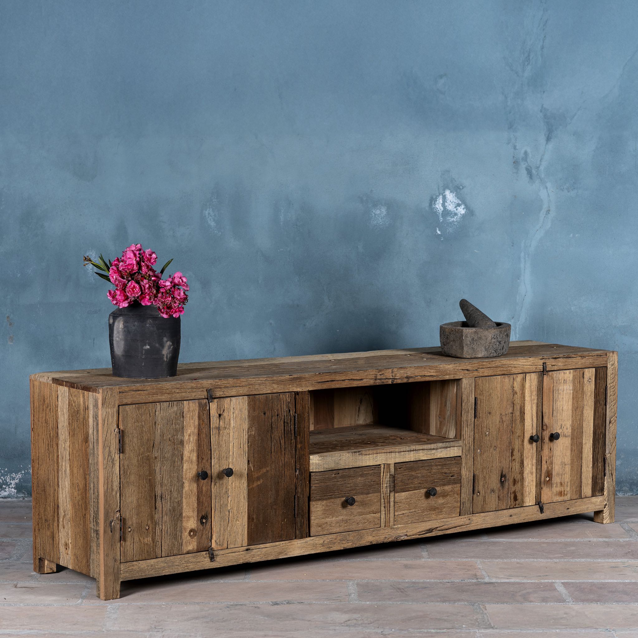 Side view image of a large sideboard in Driftwood/ Wabi Sabi style made from recycled old wood, featuring four cabinet doors, two central drawers, and an open shelf with a naturally aged, rustic finish.

