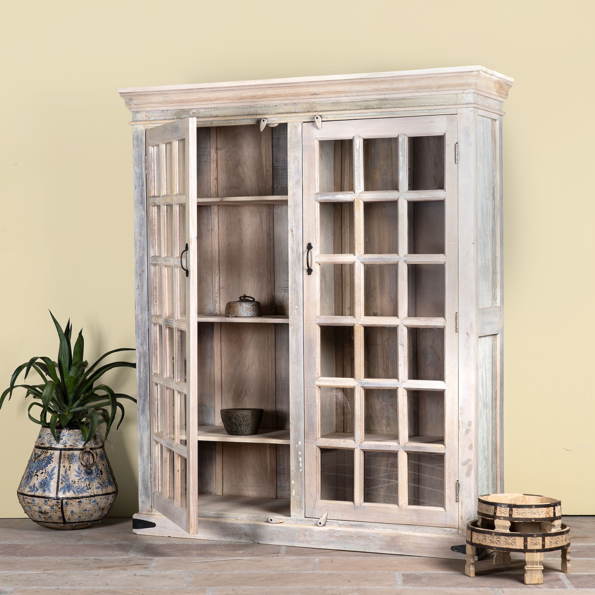 Side angle image with open door of a tall reclaimed wood cabinet in sandblasted vintage design with glass-panelled doors; rustic living room furniture, 100 × 40 × 190 cm.