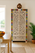 Decorative carved cabinet with colorful tile border in a room with a table and plants.