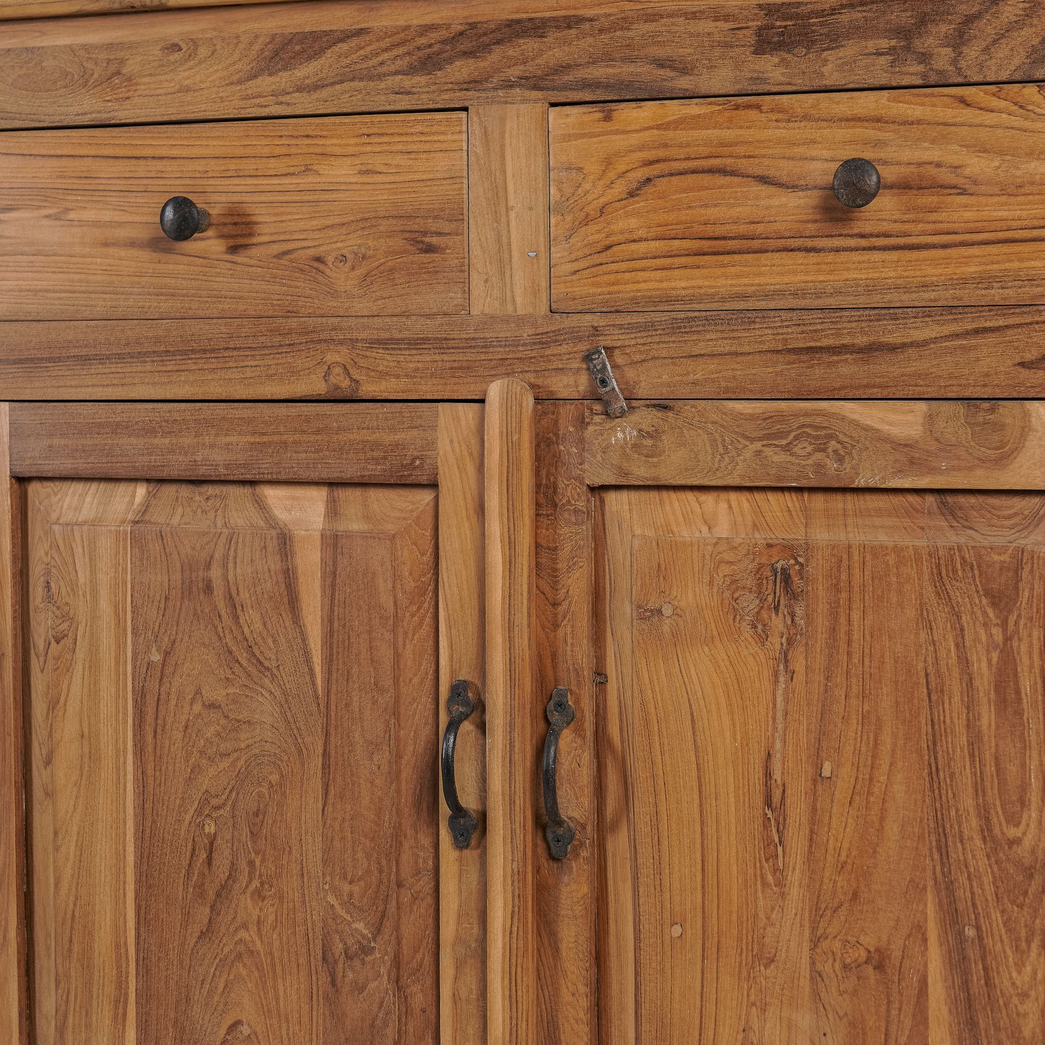 Close up image of a showcase cabinet made from reclaimed teak wood, featuring glass-panel upper doors for display, four drawers for storage, and lower cabinets with solid wood doors in a natural finish.