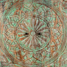 Close up image of a carved mango wood cabinet with floral hand-carving, distressed green finish, iron stand, 100 × 40 × 150 cm.