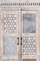 Close up image of a whitewashed mango wood cabinet with hand-carved details, rattan inserts, and glass panels; versatile as bedroom furniture or wooden wardrobe; 192 × 110 × 40 cm.
