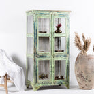 Side angle image of a refurbished teak wood showcase with distressed green finish – sustainable furniture with boho style interior appeal and glass-panelled storage.