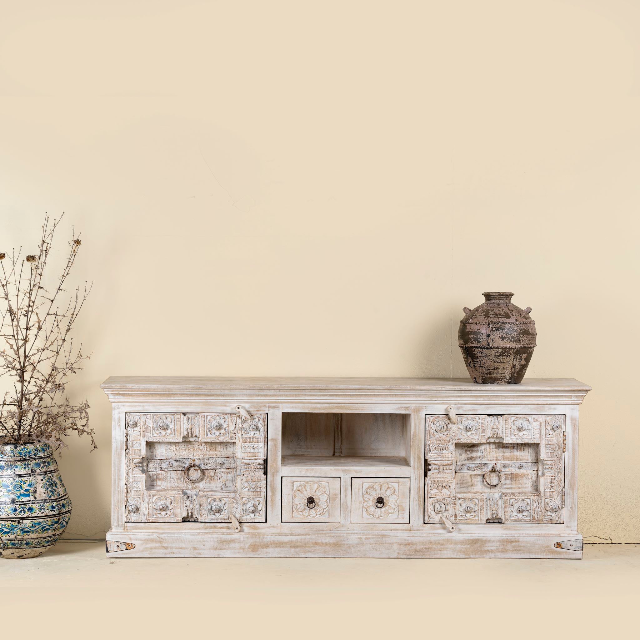 Vintage-style wooden TV stand with decorative elements against a beige wall.