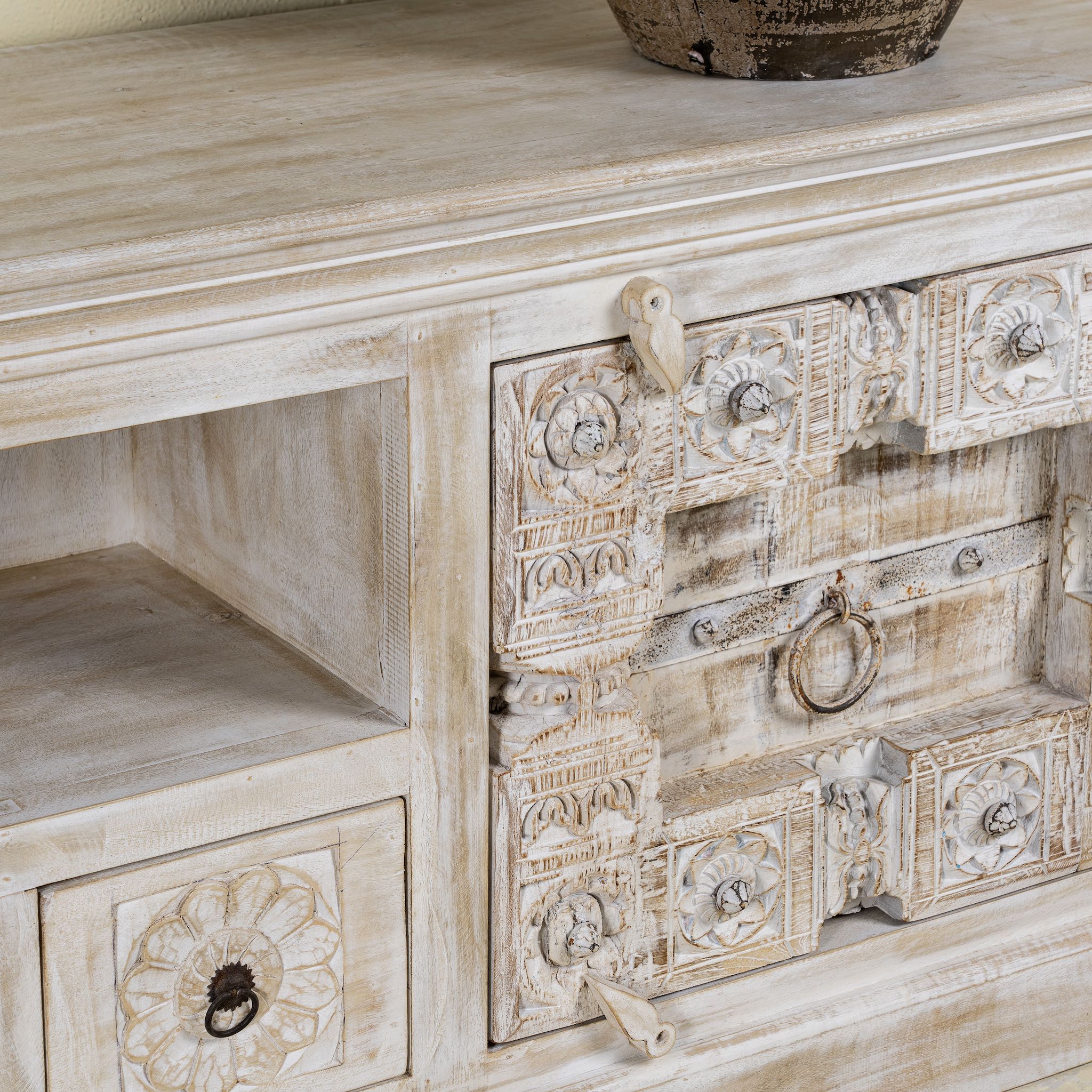 Close up picture of a low board made from reclaimed teak wood door panels, featuring detailed carvings, iron ring handles, and ample storage space in a whitewashed vintage finish.