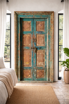 Lifestyle image of a Riddhi antique Indian door hand-carved from solid teak wood with turquoise patina and golden accents—an exquisite Indian teak wood door and architectural statement full of vintage charm.