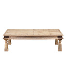 White background image of a rustic coffee table Ritvik made from old reclaimed teak wood, featuring a weathered finish, turned legs, decorative carved apron, and visible metal rivets, styled with earthy decor in a minimal interior setting.
