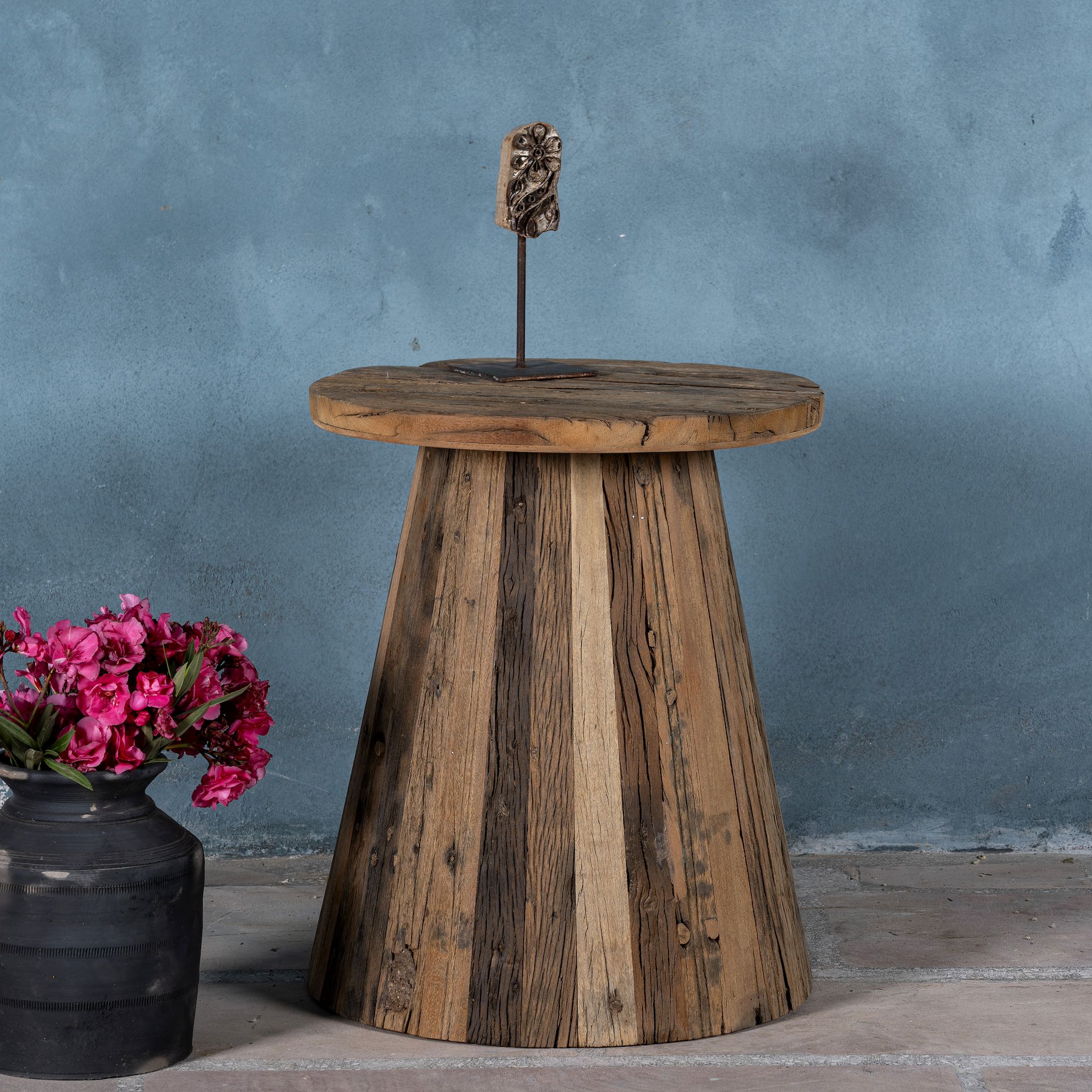 Front image of a rustic-style coffee table crafted from recycled wood, featuring a round top and tapered conical base with a natural, weathered finish showcasing varied wood tones and textures.