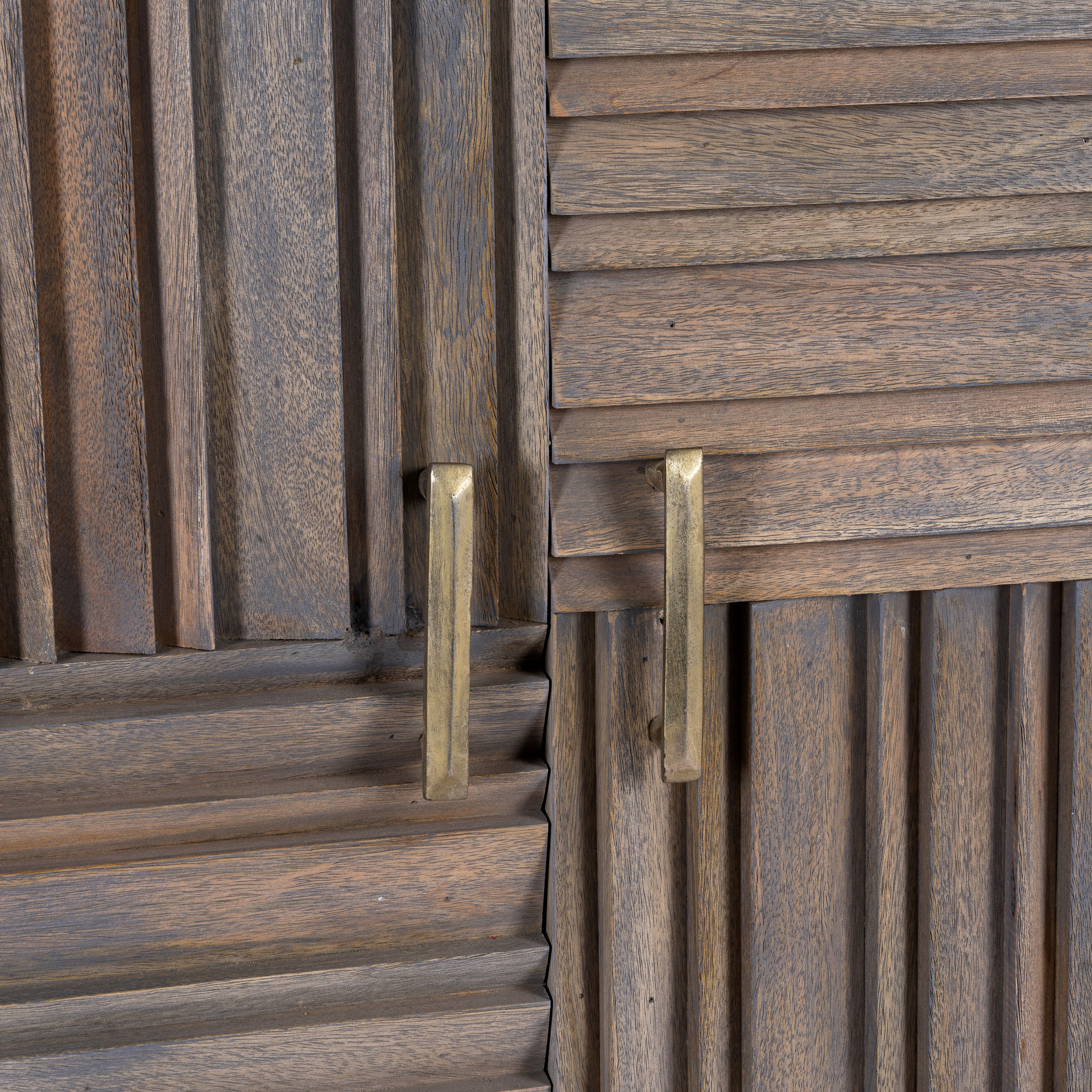 Close up image of a grey carved cabinet in mango wood with linear carvings and brass‑plated iron base, 92 × 42 × 115 cm.
