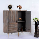 Side angle image with open door of a Grey carved cabinet in mango wood with linear carvings and brass‑plated iron base, 92 × 42 × 115 cm.