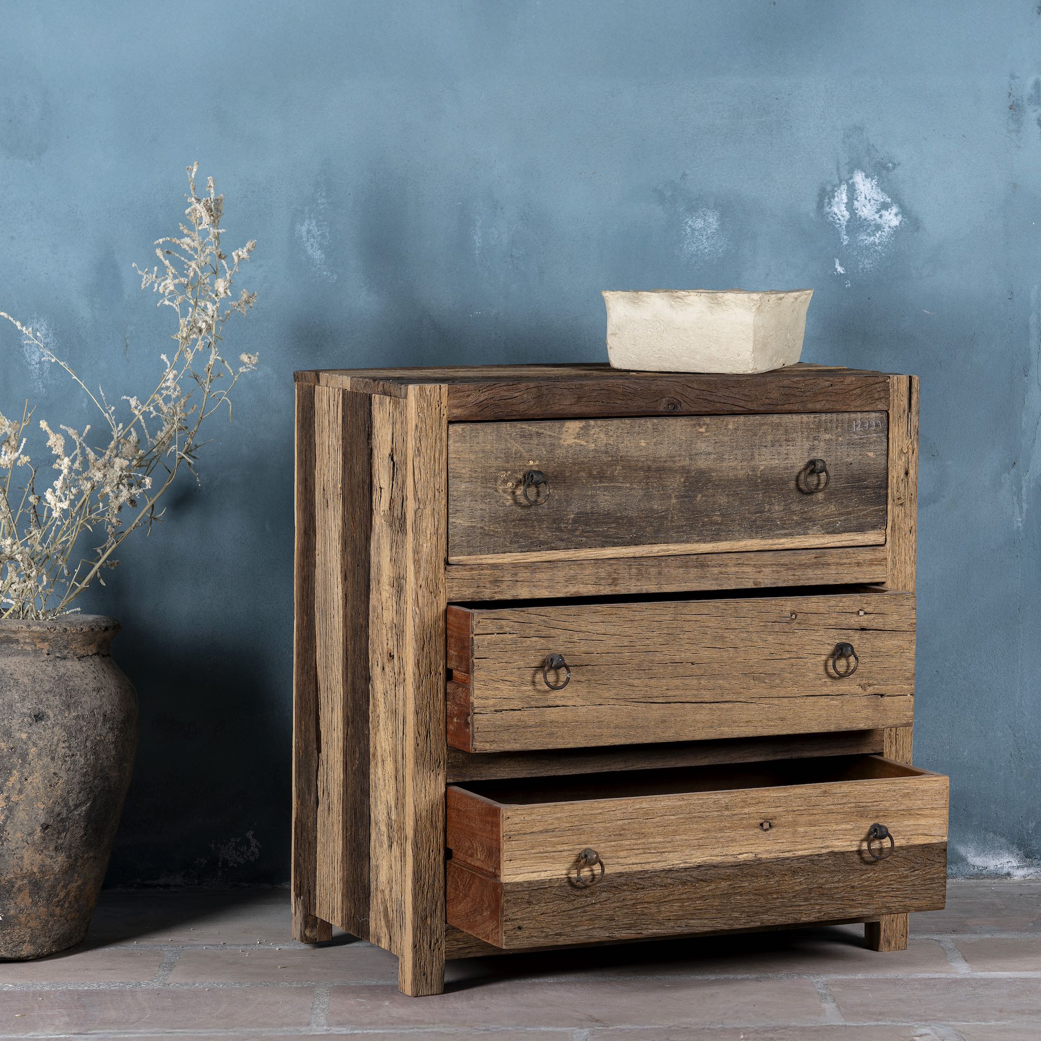 Side view image with open drawer of a three-drawer dresser in Driftwood/Wabi Sabi style made from recycled old wood, featuring a naturally weathered finish with visible grain patterns and metal ring pull handles for a rustic, handcrafted look.

