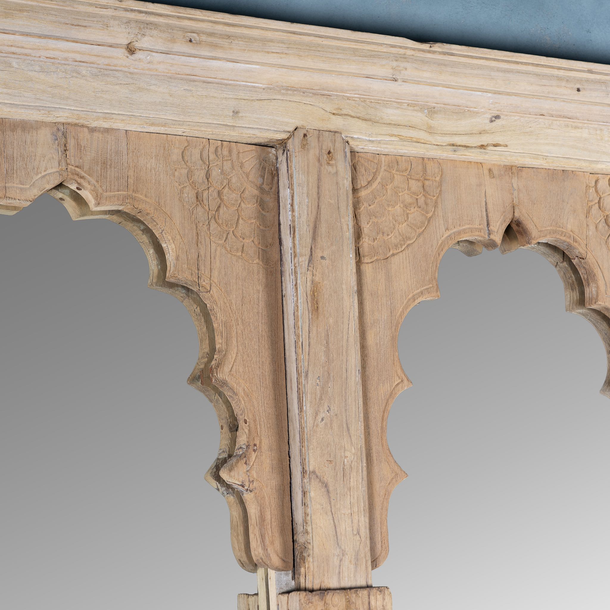 Close up picture of a tall two-arch mirror made from reclaimed natural teak wood, featuring scalloped arches and hand-carved column details in a minimalist rustic finish.
