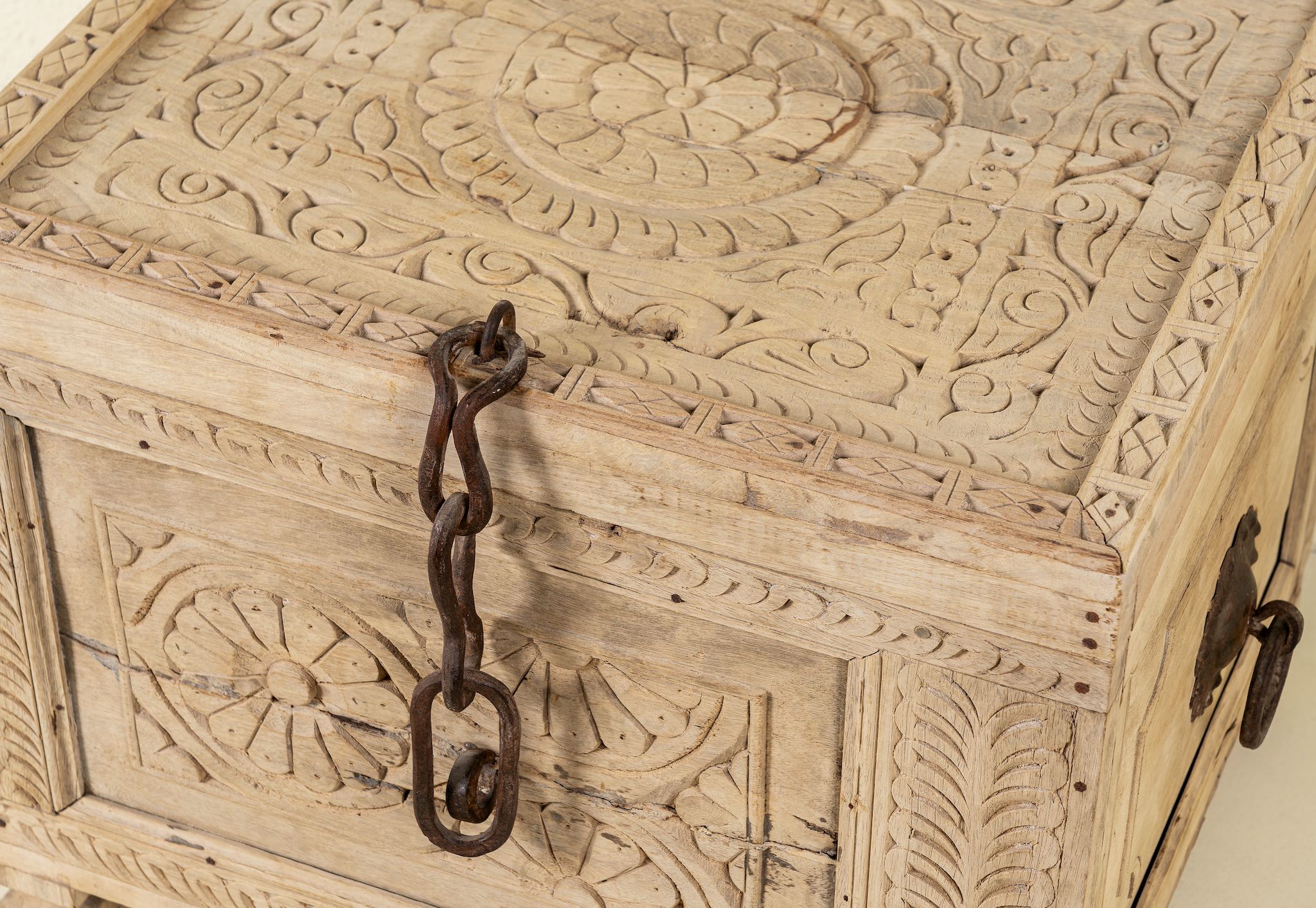 Close up image of a hand-carved storage chest made from reclaimed teak wood, showcasing intricate floral and geometric patterns on all sides, with a rustic natural finish and a vintage-style iron latch and handles.
