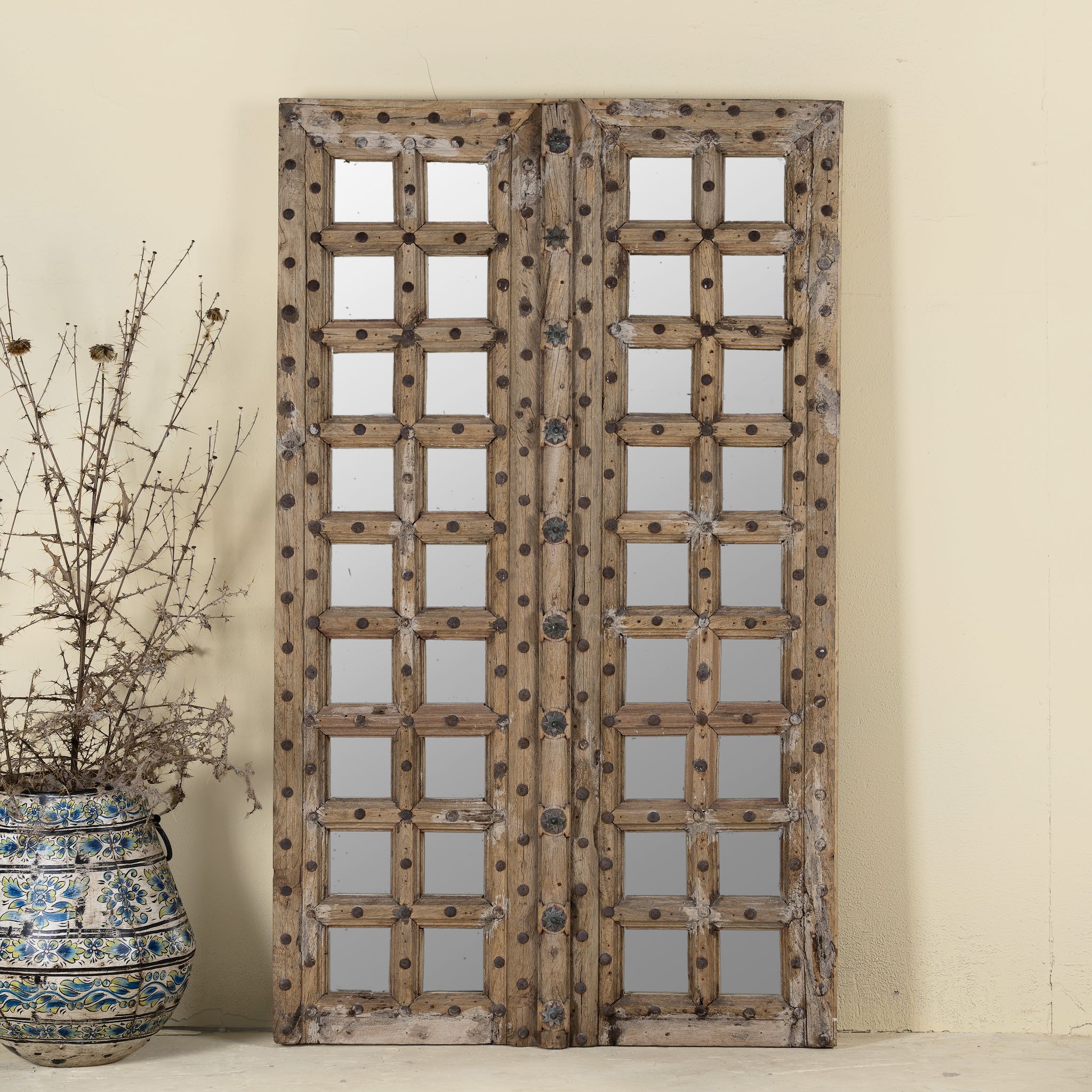 Large wall mirror made from an old teak wood door, featuring a grid of inset mirrors and rustic iron studs for a striking vintage look.