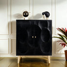 A sophisticated black mango wood cupboard with a geometric hand-carved circle design on the front, featuring a brass-plated iron stand. Decorative items are displayed on top.