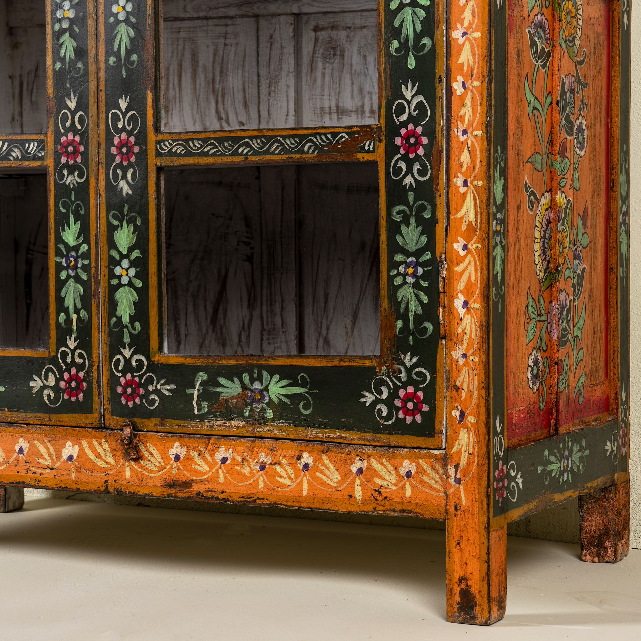 Close up image of a hand-painted reclaimed wood showcase with floral motifs and glass doors – sustainable furniture combining vintage charm and traditional craftsmanship.