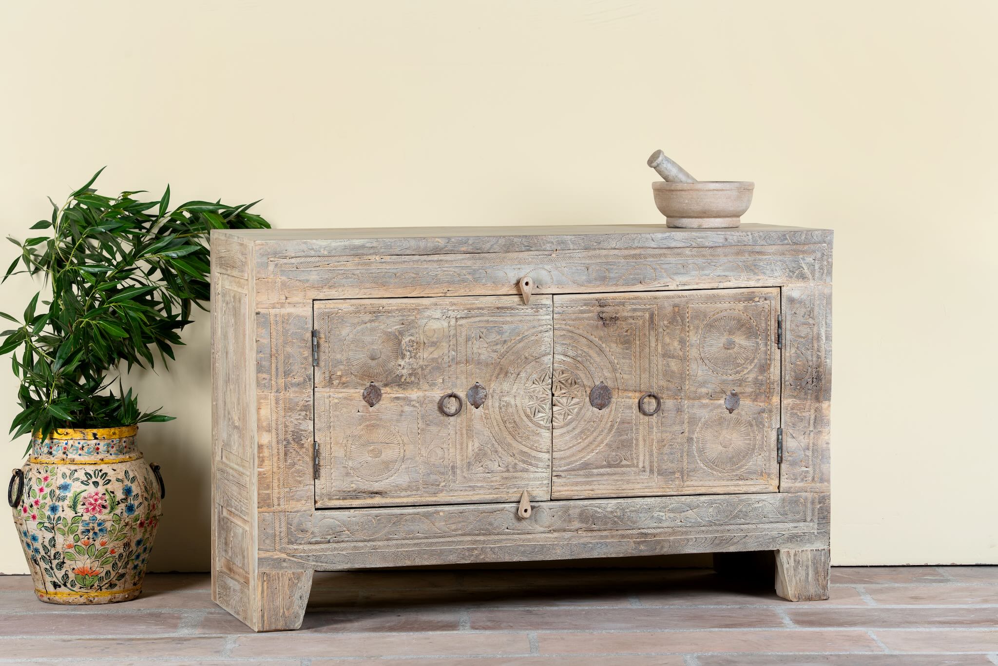 Side angle image of a handcrafted sideboard Tanay made from reclaimed teak wood, featuring antique Indian door fronts with original carvings. A Mediterranean-inspired piece of unique Indian furniture with sustainable character and functional storage.