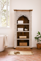 Lifestyle image of a hand-carved mango wood bookshelf with arched frame and whitewashed finish – carved wooden furniture and mango wood shelving with Indian-inspired design.