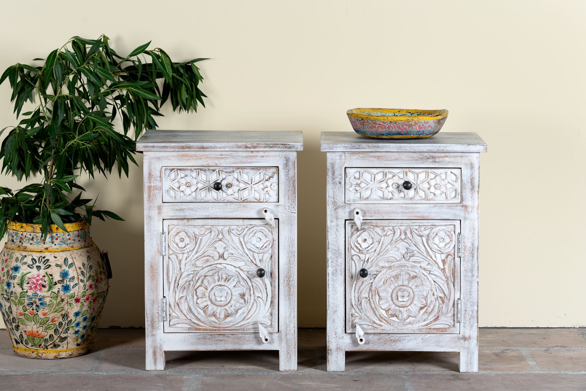 Pair of mango wood nightstands Uday with whitewashed vintage finish, featuring hand-carved geometric and floral designs. Each bedside table includes a drawer and cabinet for elegant and practical storage.