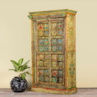 Side angle image of a hand painted wardrobe made of teak wood with floral motifs; unique furniture inspired by Indian artistry, 104 × 50 × 186 cm.
