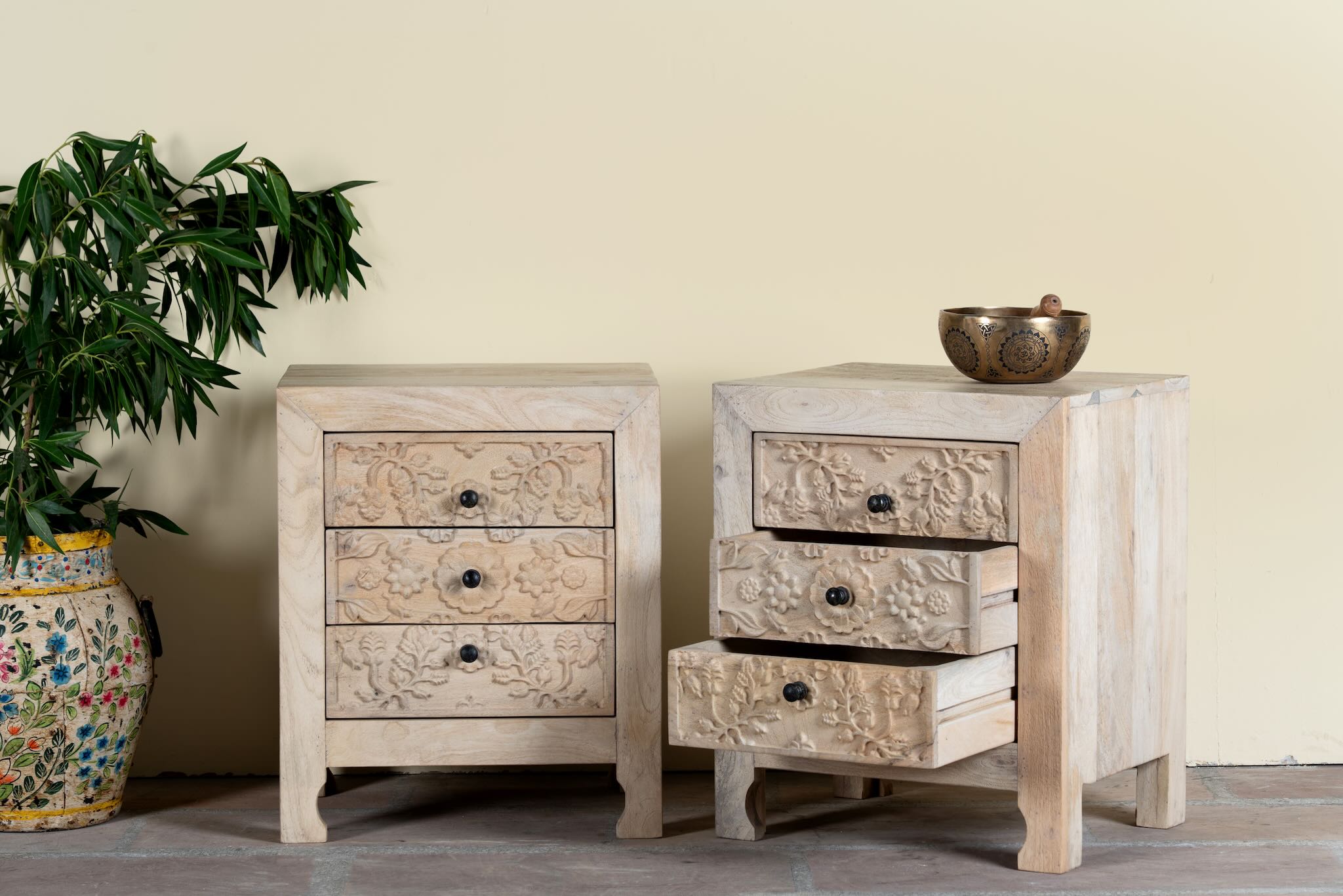 Side angle image with open drawers of a pair of mango wood nightstands Vihaan with hand-carved floral drawer fronts and a natural distressed finish. Elegant vintage-style bedside tables offering both storage and artisan-crafted detail.