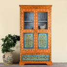 Lifestyle image of a hand-painted teak wood showcase with floral motifs and glass doors – sustainable furniture crafted from recycled wood with traditional Indian artistry.