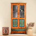 A hand-painted reclaimed wood Boho showcase with intricate floral patterns, made from refurbished teak wood, with glass doors and shelves.
