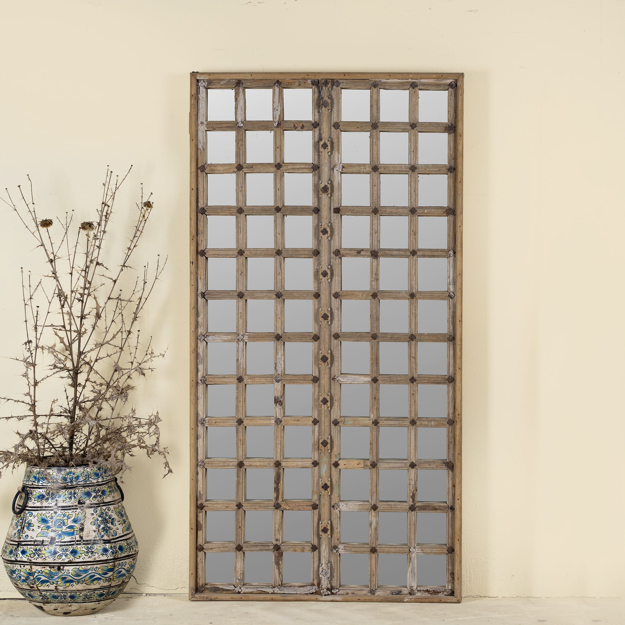 Wall mirror crafted from an old teak window frame with a fine grid of small mirrored panes and rustic metal accents, blending heritage with minimalist design.