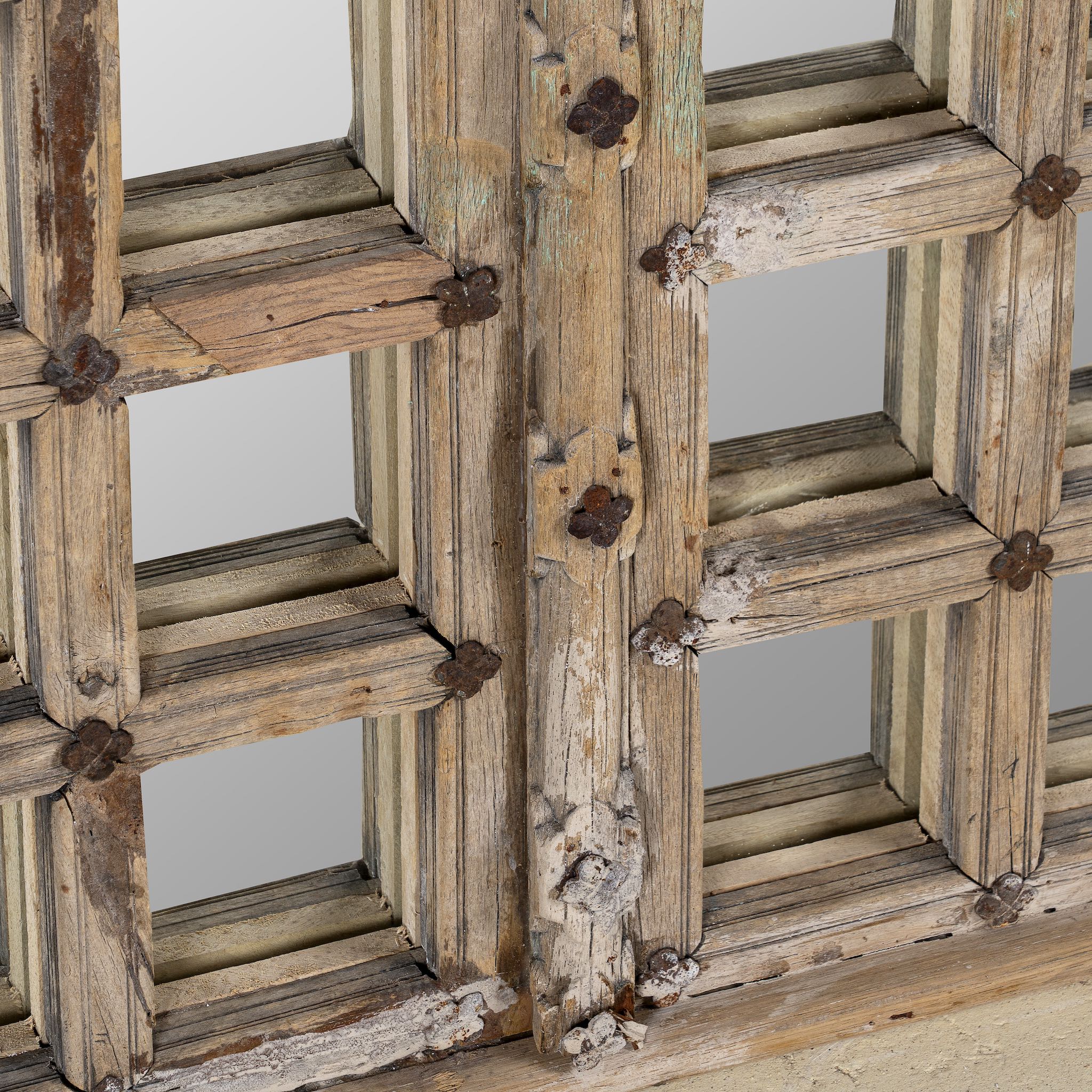 Close up of a wall mirror crafted from an old teak window frame with a fine grid of small mirrored panes and rustic metal accents, blending heritage with minimalist design.