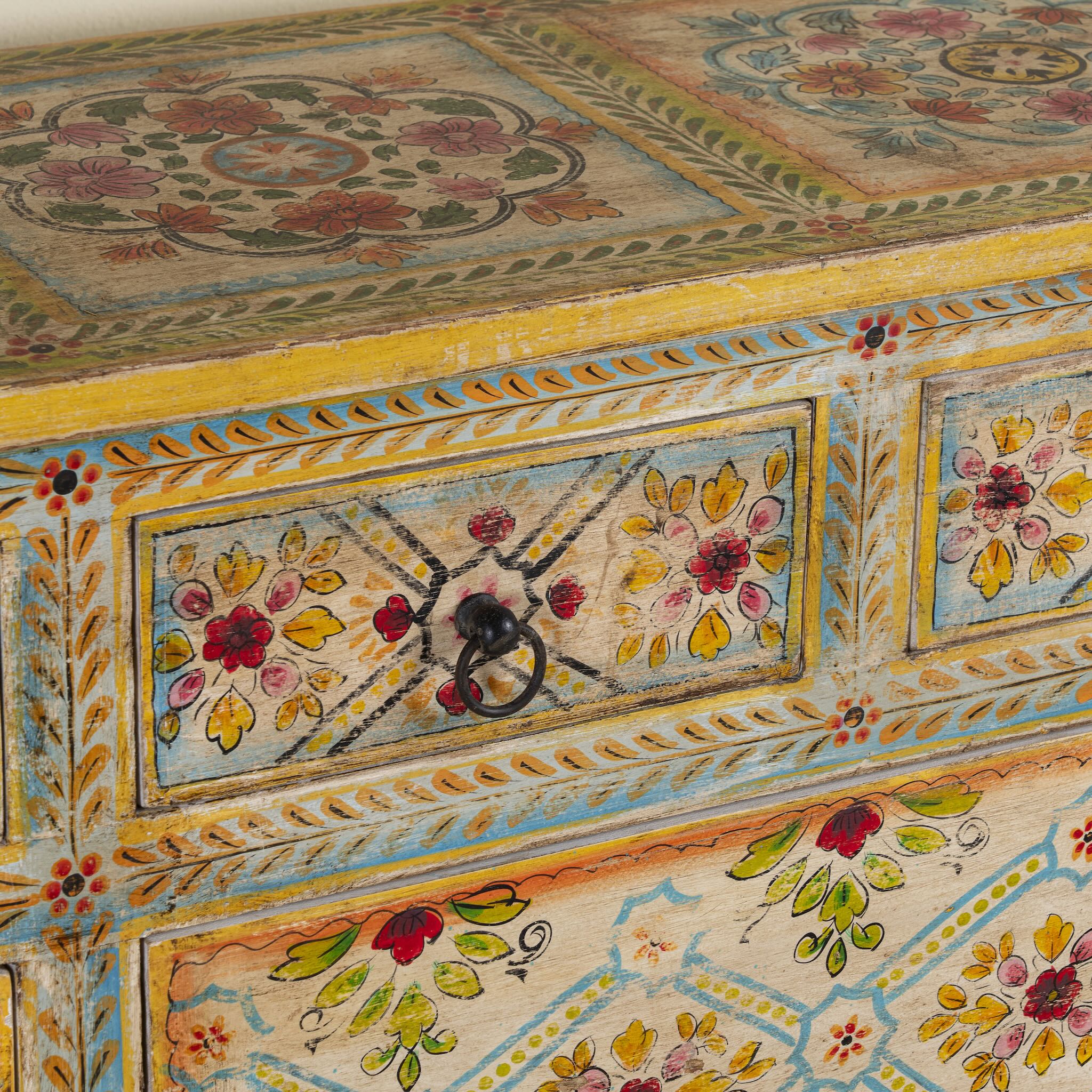 Close up image of a Ziya hand‑painted chest of 8 drawers made from reclaimed wood with floral motifs and iron handles—an artisan piece of painted wooden furniture.