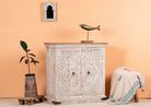 Side angle image of a whitewashed mango wood sideboard with hand-carved floral patterns; compact carved sideboard for vintage interiors, 90 × 90 × 40 cm.
