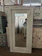 Warehouse pic of a tall white washed wall mirror with hand carved wooden mango wood frame; 180 × 90 × 10 cm.