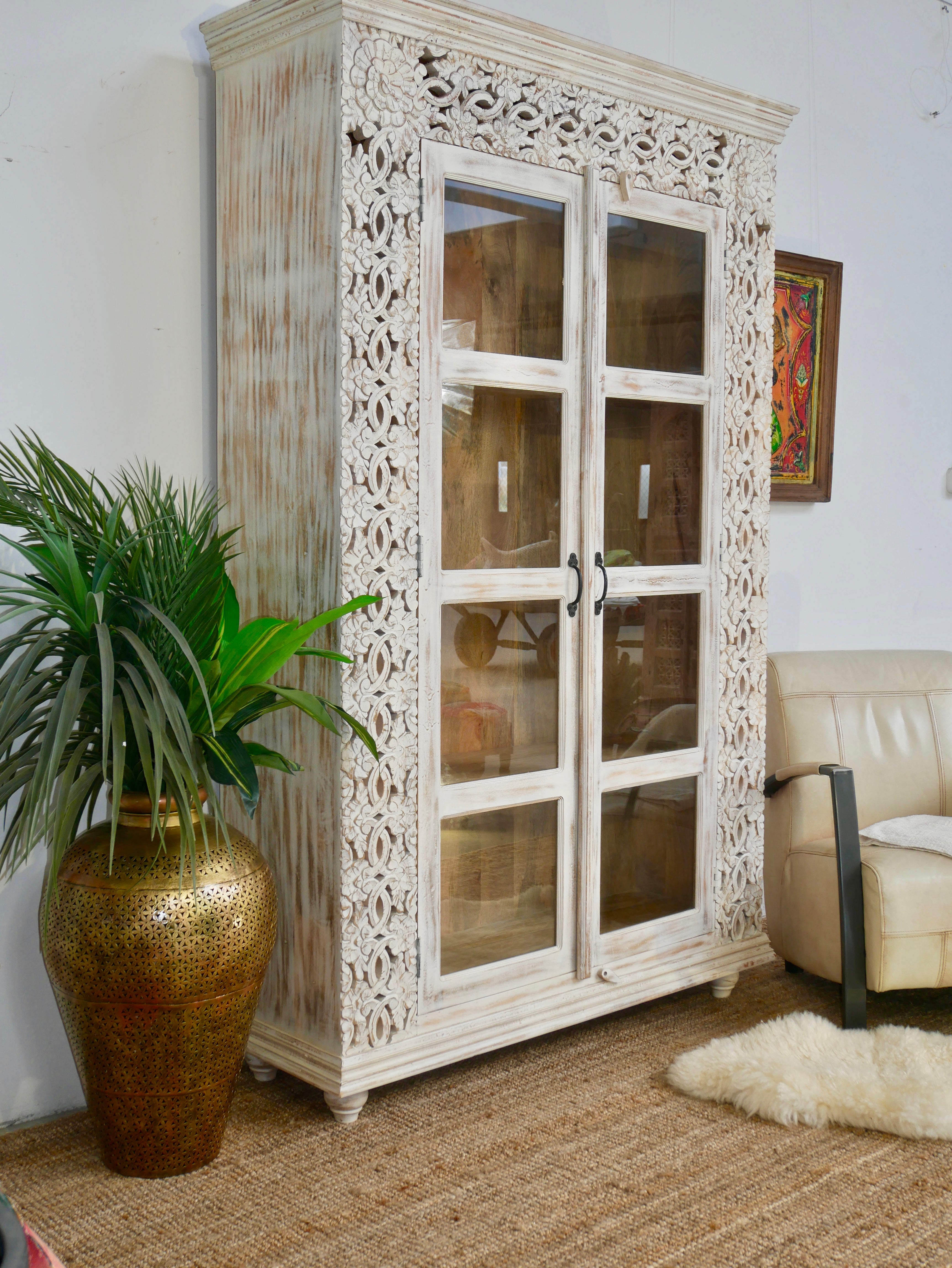 Side angle image of a handcrafted mango wood cabinet with glass-panelled doors and internal storage – carved wood furniture made from sustainable mango wood with unique natural grain.